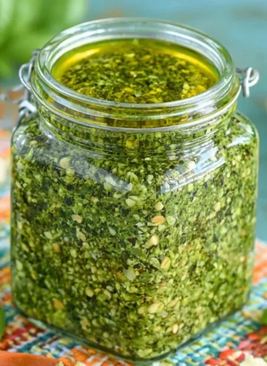 Fresh basil pesto sauce in a bowl with basil leaves and pine nuts.