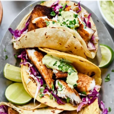 Blackened fish tacos topped with avocado cream sauce on a plate