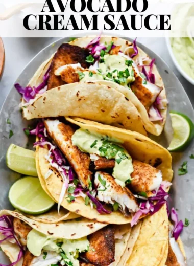 Blackened fish tacos topped with avocado cream sauce on a plate