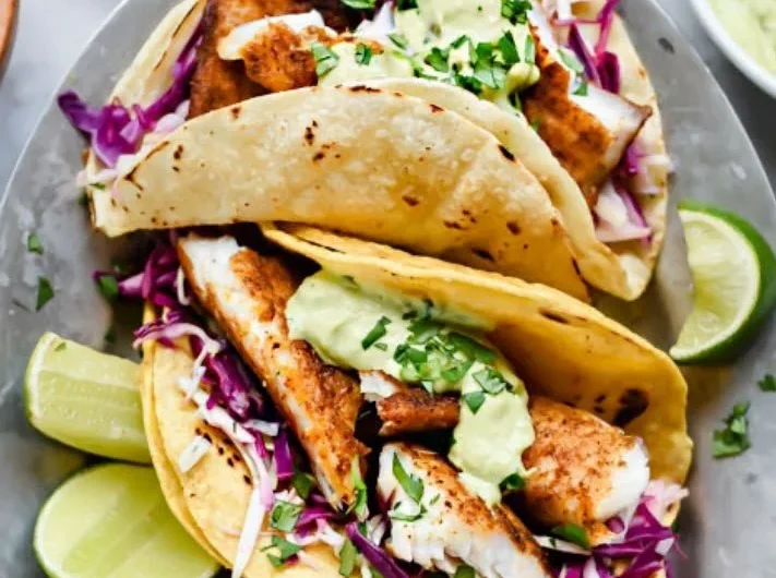 Blackened fish tacos topped with avocado cream sauce on a plate