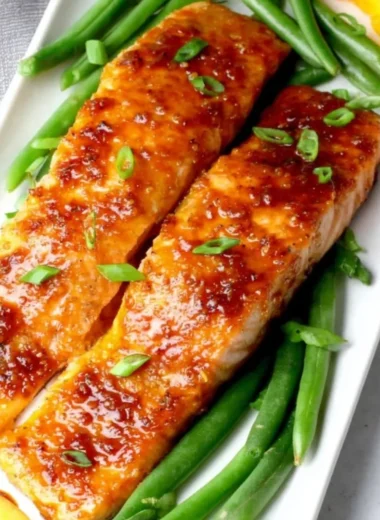 Peach glazed salmon fillet garnished with fresh herbs on a plate.